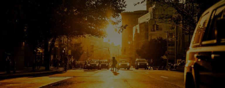People crossing a busy road at sunset - the image is very orange and yellow - shot in the centre of the road.