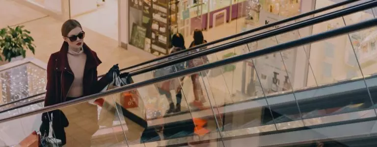 A woman with shopping going up an escalator in a retail store