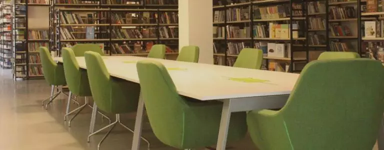 A table with green chairs inside a library 